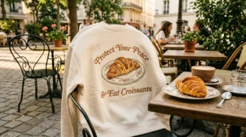 The Croissanterie inspired Protect Your Peace embroidered cream sweatshirt on a bistro chair