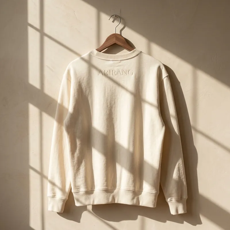 BTS Members Reunite: 'ARIRANG' Comeback & Subtle Merch Fashion A candid lifestyle photo of a young woman wearing the cream Arirang embroidered sweatshirt, laughing with friends at a coffee shop while watching a video on her phone.