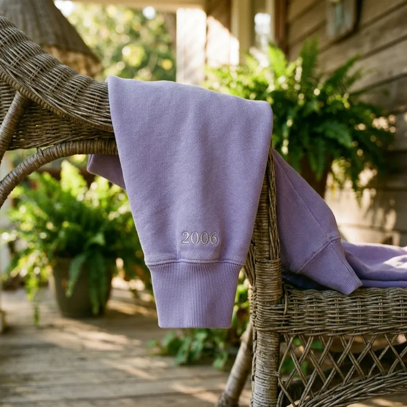 A candid lifestyle shot of a young woman in her late 20s wearing the vintage lavender Y2K Pop Star Embroidered Crewneck, laughing while holding a coffee cup in a sunlit, cozy cafe setting.
