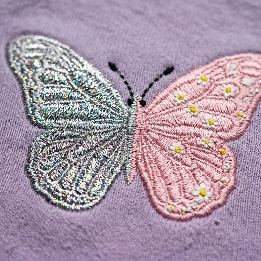 A close-up detail shot of the left cuff of the lavender sweatshirt, showing the year '2006' elegantly embroidered in tiny, shimmering silver thread.