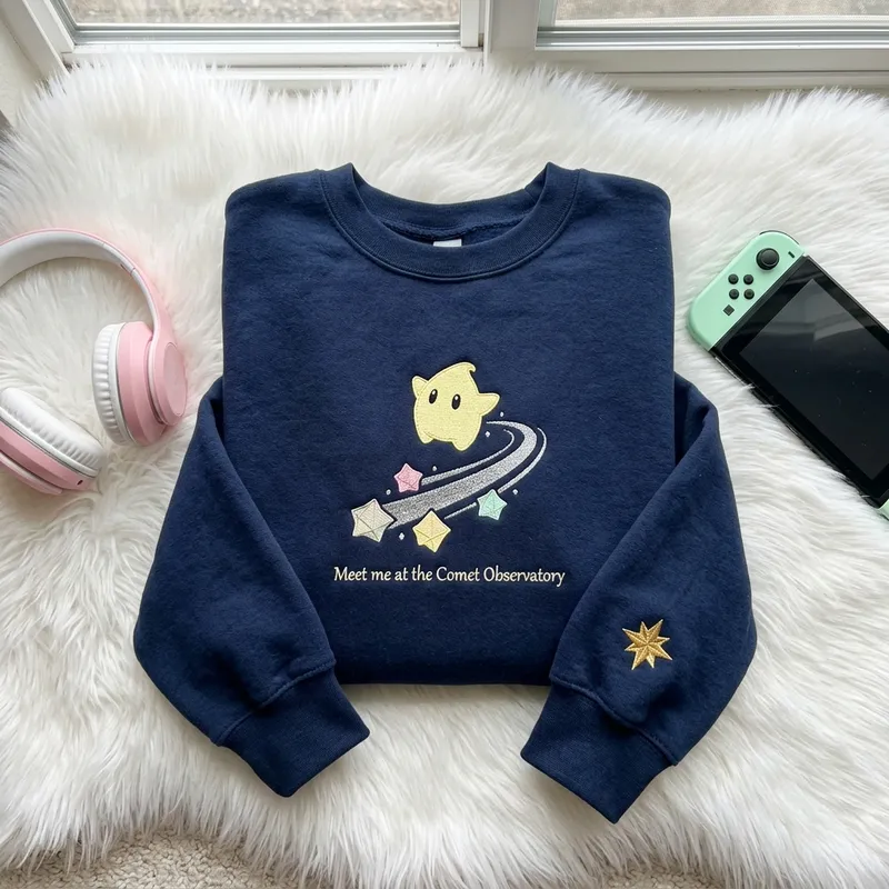 Super Mario Galaxy Movie: Fan Backlash & Cozy Apparel Close-up macro shot showing the pristine embroidery stitch detail of the lemon-chiffon Luma and metallic silver thread on the custom sweatshirt