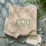 Frog Sweatshirt - Whimsical Dancing Frogs Trio Embroidered Sweatshirt, Sand Cottagecore Apparel embroidered-sweatshirt
